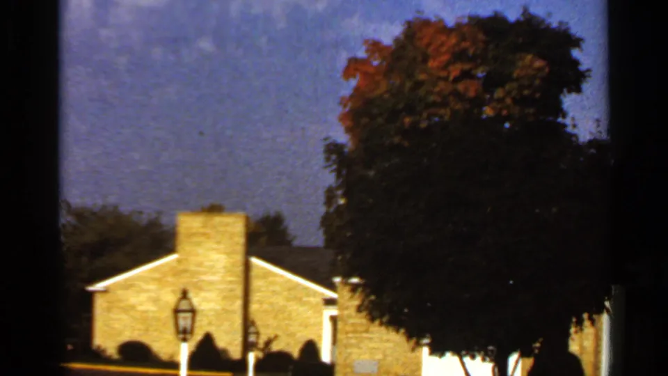 1966 St. Louis-area 8mm frame showing a brick suburban house, chimney, lantern-style yard lamp, and dark autumn tree.