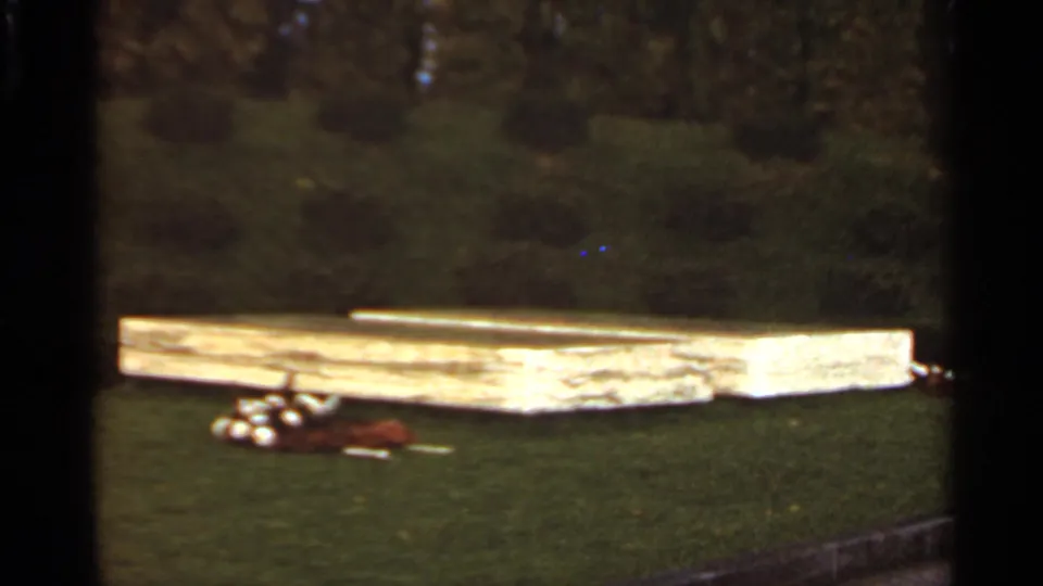 1966 Saint Louis home-movie frame showing a wooden platform across the lawn, with clustered golf balls and a brown bag in the foreground.