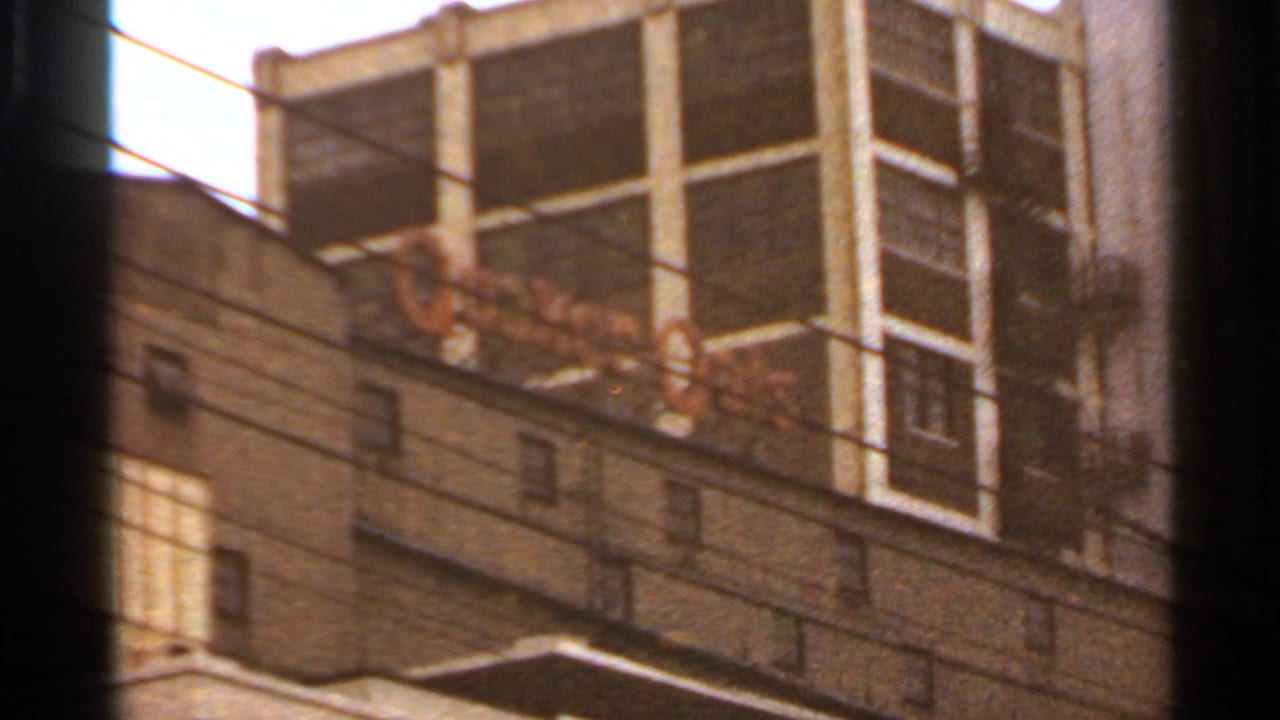 1966 Saint Louis frame with a white grid-like high-rise behind a lower masonry building, seen through soft handheld 8mm framing.