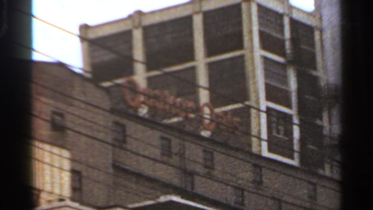 Handheld 1966 Saint Louis view of a large white grid-like building rising behind a lower masonry exterior and utility wires.