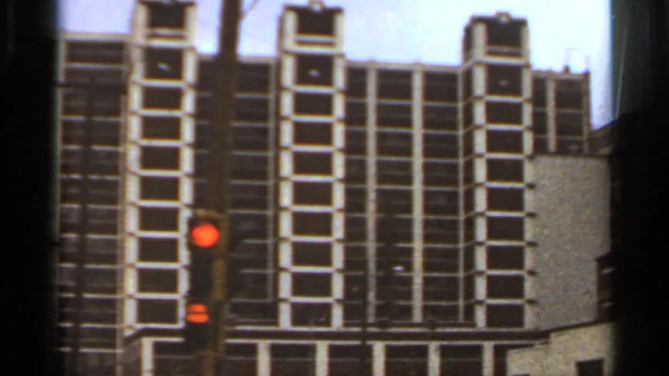 Saint Louis high-rise facade on 8mm film, seen with dark window bands and a red traffic signal in the foreground.