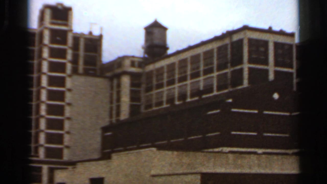 Multi-story yellow and brown building with a rooftop water tower under cloudy sky.