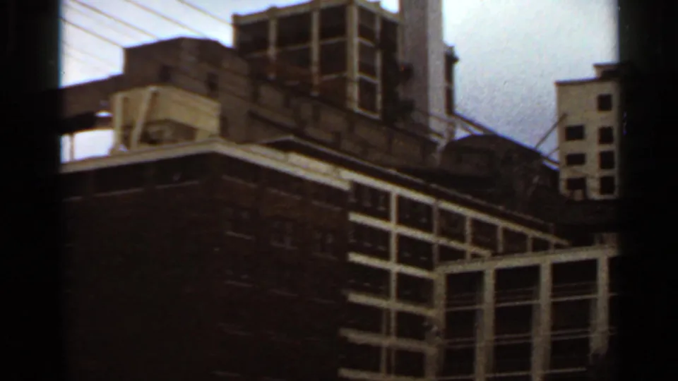 1966 Saint Louis handheld view looking across a low masonry building toward taller urban structures and overhead utility wires.