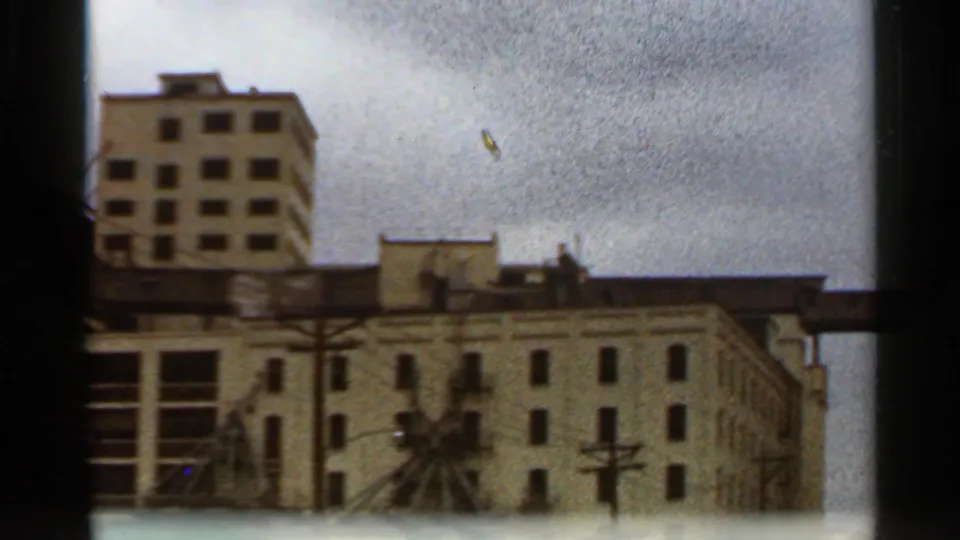 1966 Saint Louis street-facing view of layered urban buildings, utility poles, overhead wires, and a pale multi-story structure behind them.