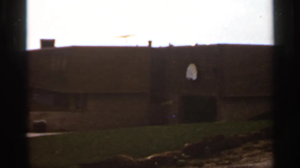 1966 Saint Louis 8mm view of a brick school wall, basketball hoop, lawn, roof antenna, and overexposed sky.
