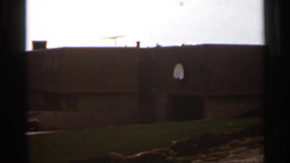 1966 Saint Louis exterior frame showing a brick school building, basketball hoop, lawn, roofline, and bright sky.