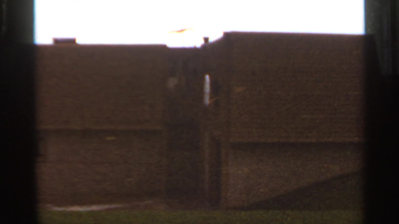 Saint Louis 1966 8mm frame showing a dim building exterior, roofline, chimney detail, and grassy slope with strong film grain.