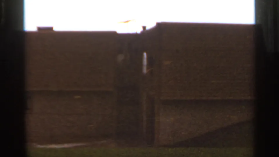 Saint Louis 1966 8mm frame showing a dim building exterior, roofline, chimney detail, and grassy slope with strong film grain.