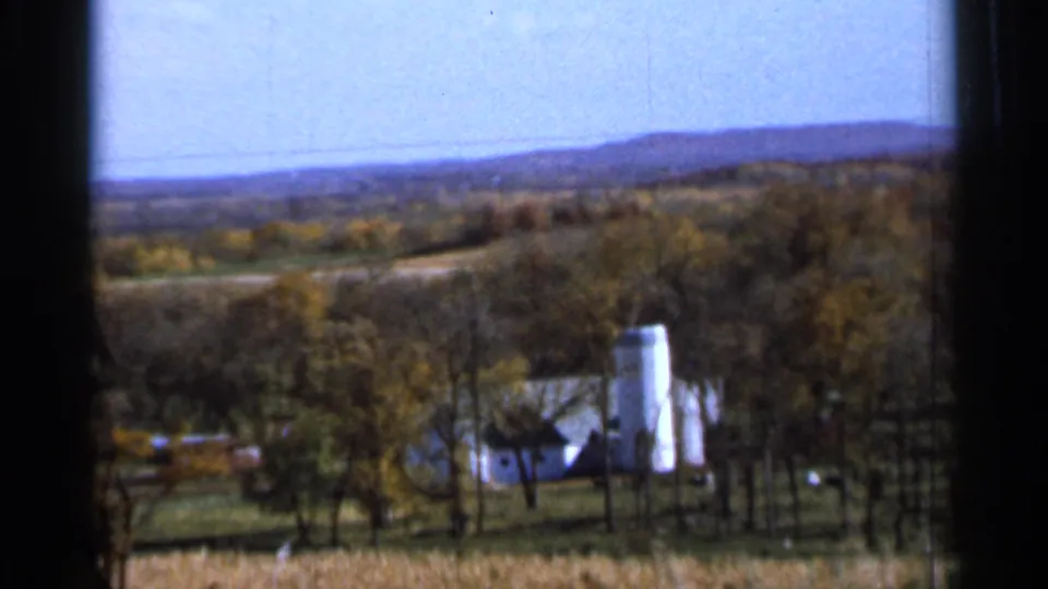 1966 rural Sauk Centre view across trees and fields toward a small farmstead with a white silo and distant hills.