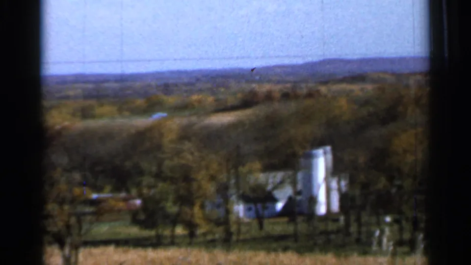 1966 8mm view near Sauk Centre, Minnesota, showing a distant white farmhouse, silo, fields, trees, and window framing.