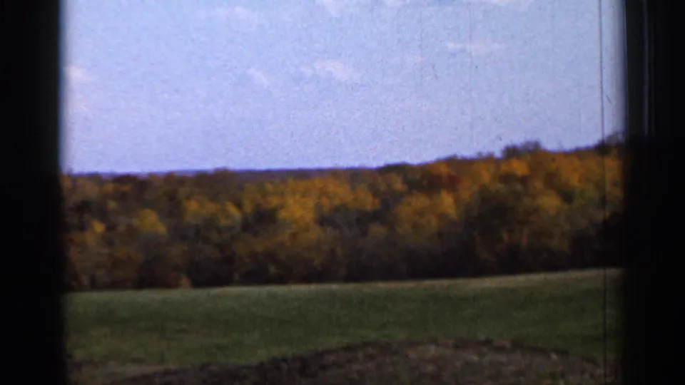 1966 8mm countryside view near Sauk Centre with open field, autumn foliage, low hill, pale sky, and window-edge framing.