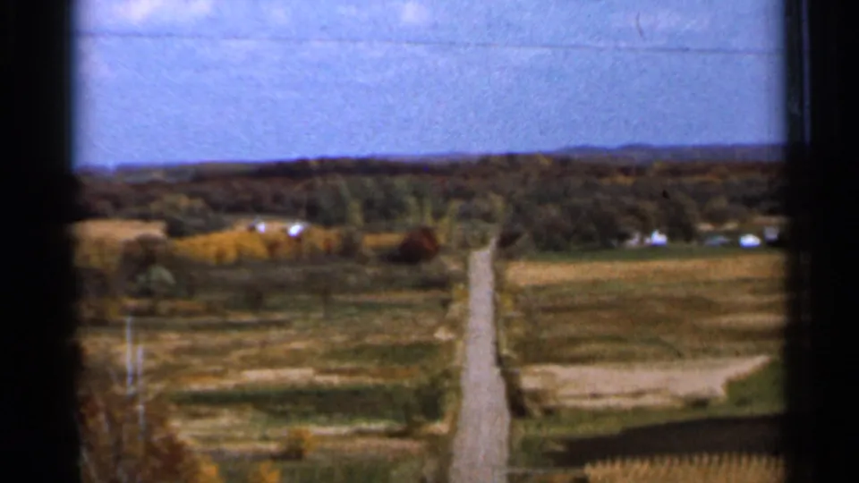 1966 Sauk Centre area countryside showing a narrow road or farm lane, patchwork fields, distant buildings, tree lines, and horizon.