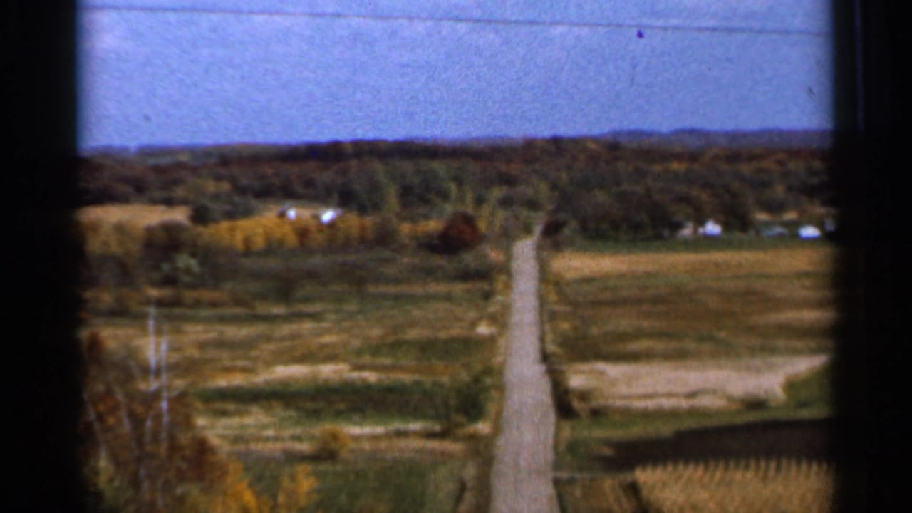 Country road and patchwork fields with distant houses and tree line.