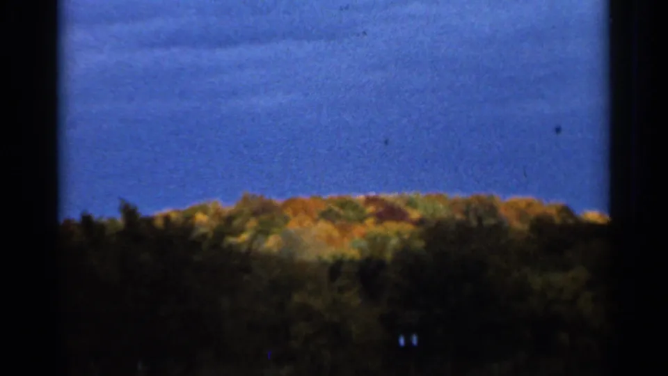 1966 Sauk Centre, Minnesota frame with a distant band of autumn trees, dark foreground, and clear blue sky.