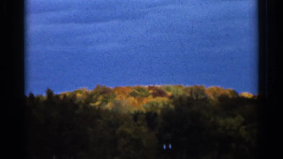 1966 Sauk Centre, Minnesota 8mm frame looking through a dark window border toward fall-colored trees and a blue sky.