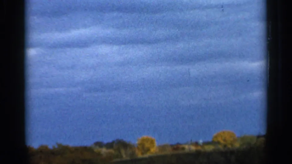Sauk Centre 1966 8mm frame with a lower horizon, scattered trees, and blue sky seen past dark window framing.