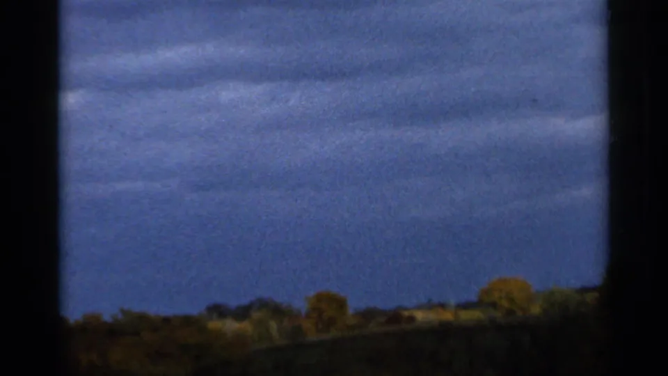 Final 1966 Sauk Centre frame showing cloud bands, dark window edging, and a low autumn treeline in soft 8mm color.