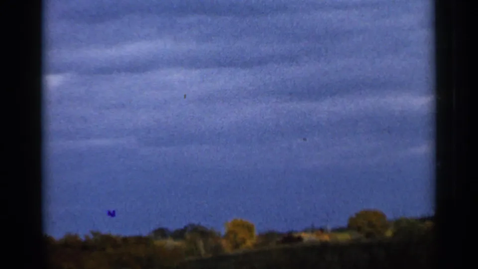 1966 Sauk Centre 8mm frame showing a dark blue-gray sky over distant autumn trees and low rural field.