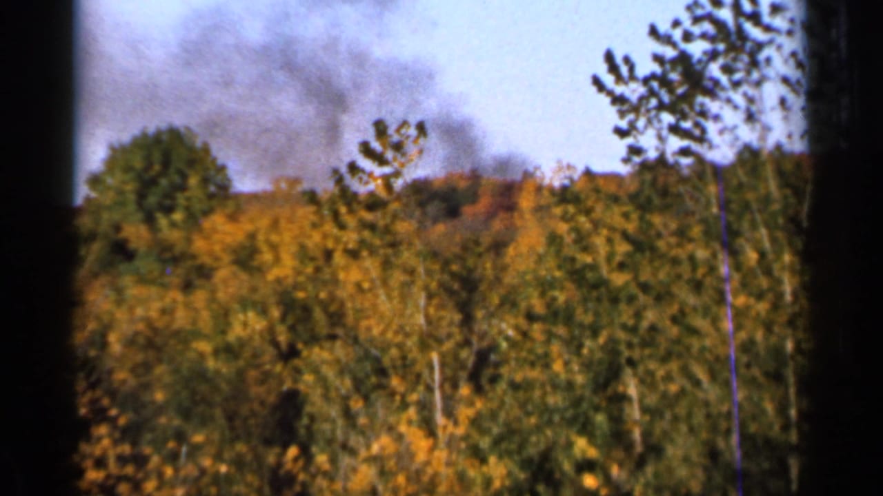 1966 Sauk Centre, Minnesota 8mm frame showing dark smoke beyond yellow-orange autumn trees under a hazy sky.