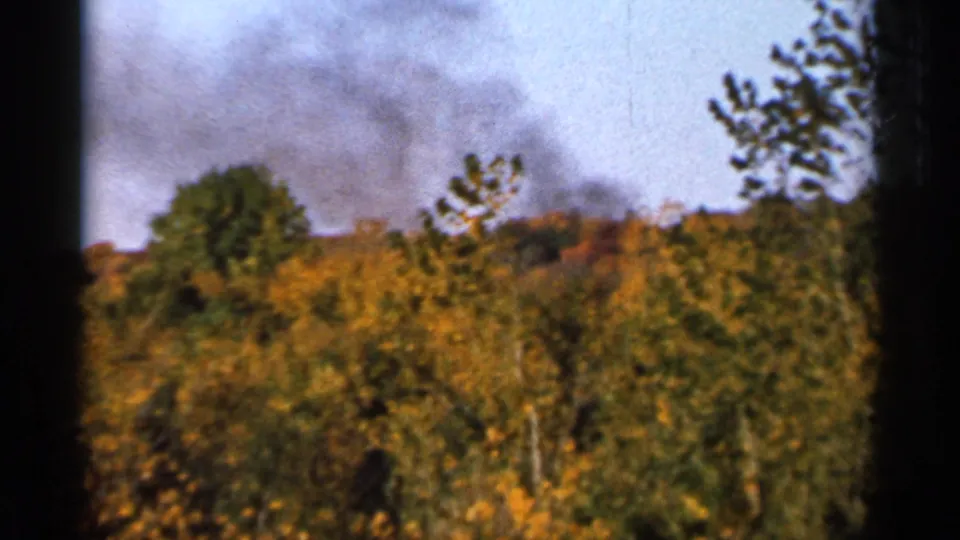 Distant smoke drifts over autumn woods in Sauk Centre, Minnesota, seen through soft 8mm home-movie framing.