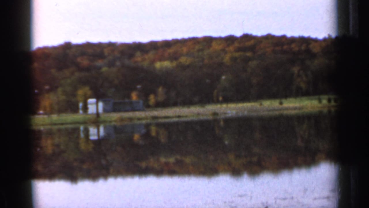 Lake reflecting a wooded hillside with shoreline structures in soft 8mm focus.