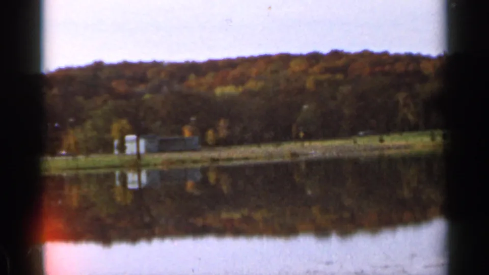 Sauk Centre lakeside scenery with wooded shoreline and autumn colors mirrored in calm water on 8mm film.