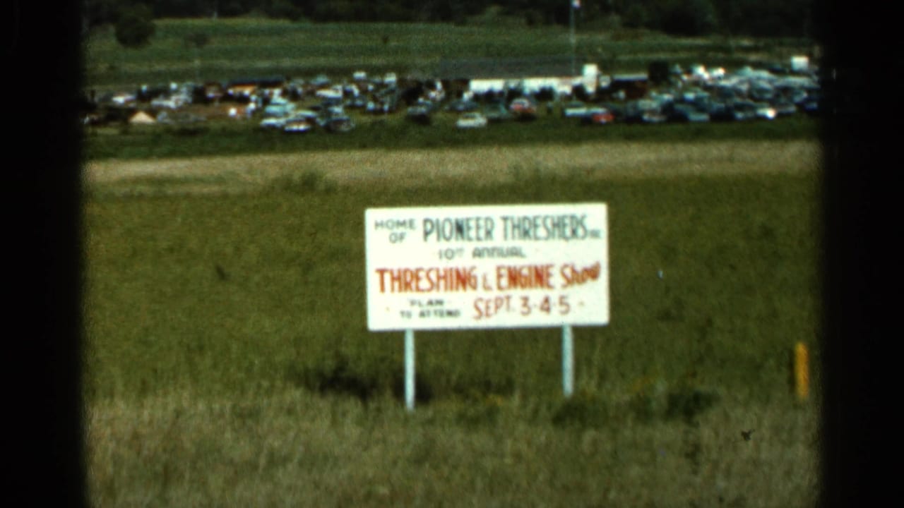 White Threshing and Engine Show sign in a grassy field with cars in the distance.
