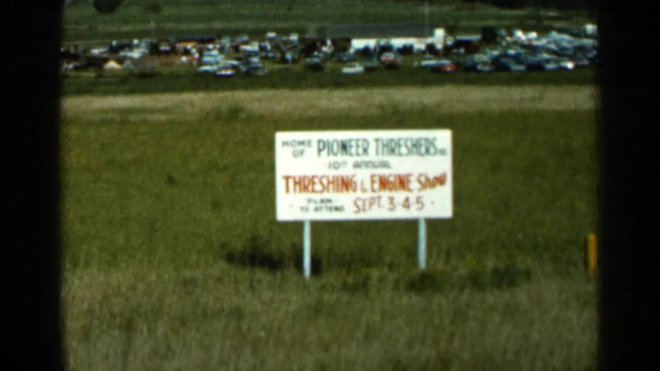 1966 Wauseon, Ohio home-movie frame showing the Threshing and Engine Show sign below a distant line of parked cars.