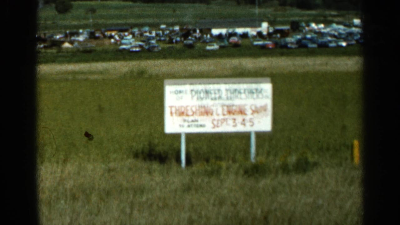 1966 Wauseon, Ohio home-movie frame showing a Threshing and Engine Show sign in grass with rows of parked cars beyond.