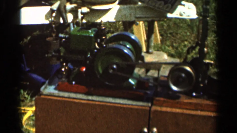 Close-up of a small green model steam engine or farm engine display with exposed belts, wheels, and mechanical fittings.