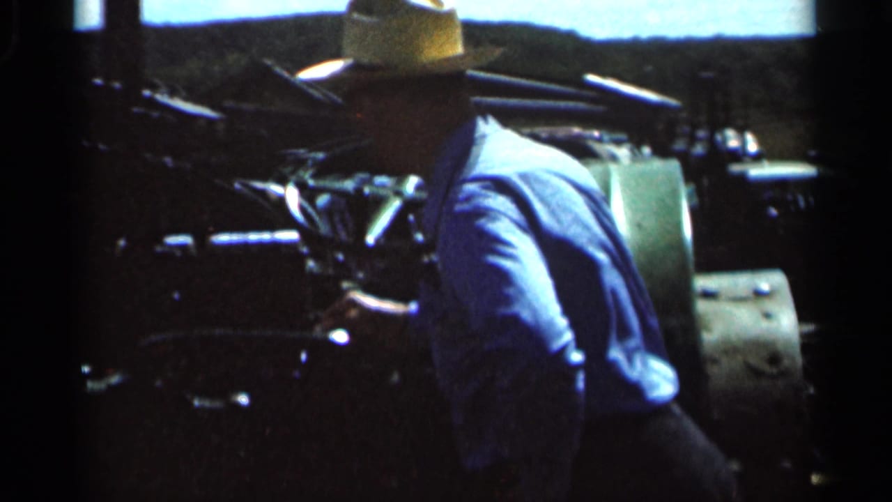 Man in straw hat and blue shirt seated at a vintage tractor in open countryside.