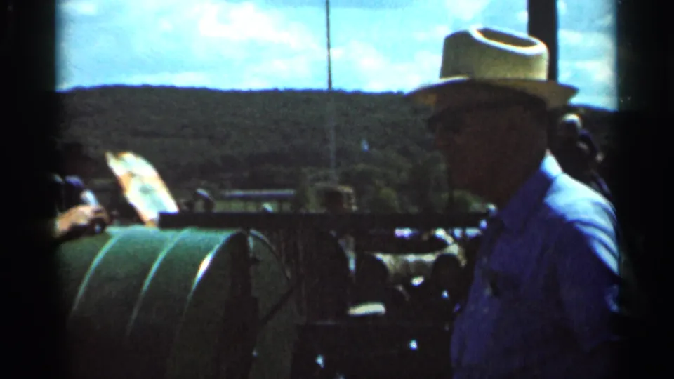 A straw-hatted man wearing sunglasses is seen beside the green tractor in the Wauseon, Ohio countryside footage.