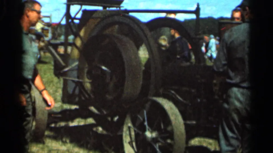Men in work clothes gather near a large vintage tractor wheel in rural Wauseon, Ohio, in 1966 home-movie footage.