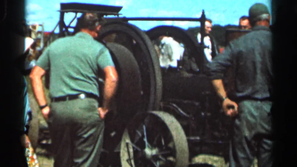 Adult fairgoers in 1960s casual clothing stand around a steam tractor in Wauseon, Ohio, with the engine filling the frame.