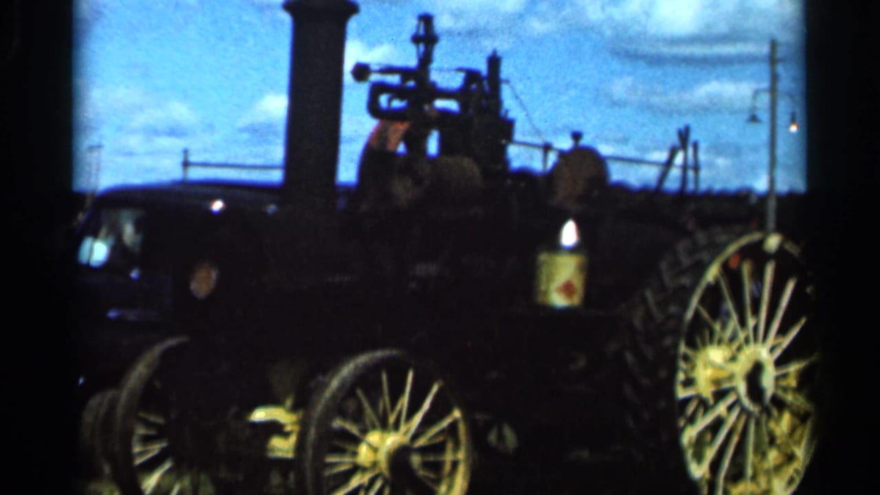 1966 Wauseon, Ohio home-movie frame showing a dark steam engine with large spoked wheels, smokestack, and bright summer sky.