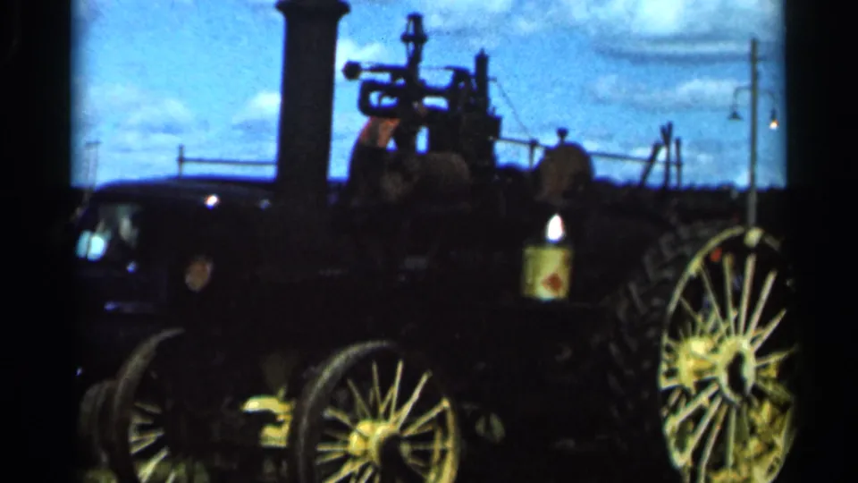 1966 Wauseon, Ohio home-movie frame showing a dark steam engine with large spoked wheels, smokestack, and bright summer sky.