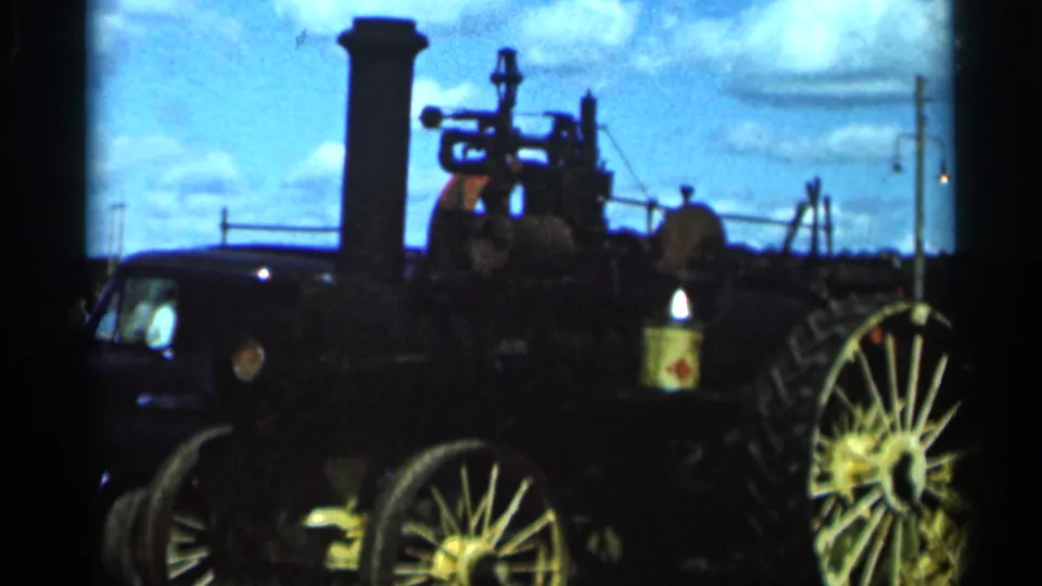 Side view of an old steam engine in Wauseon, Ohio, with a tall stack, metal fittings, and a large spoked wheel in 8mm color.