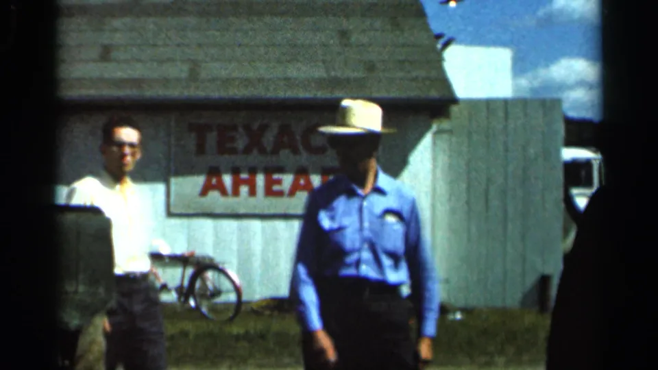 Two men in summer clothing stand near the engine in 1966 Wauseon, Ohio, with a painted Texaco sign and bicycle visible behind them.