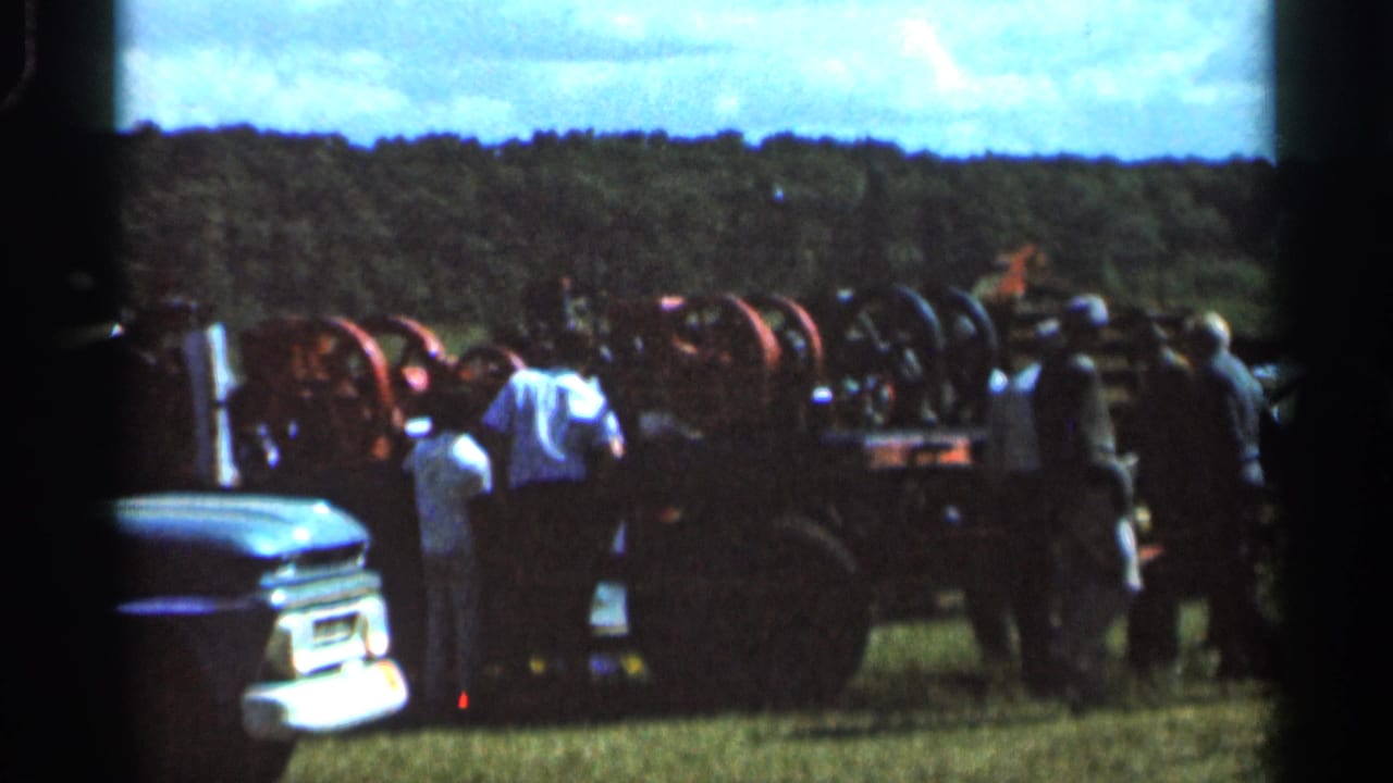 1966 Wauseon, Ohio 8mm frame showing spectators clustered around steam-powered machinery beside an older car in a grassy field.