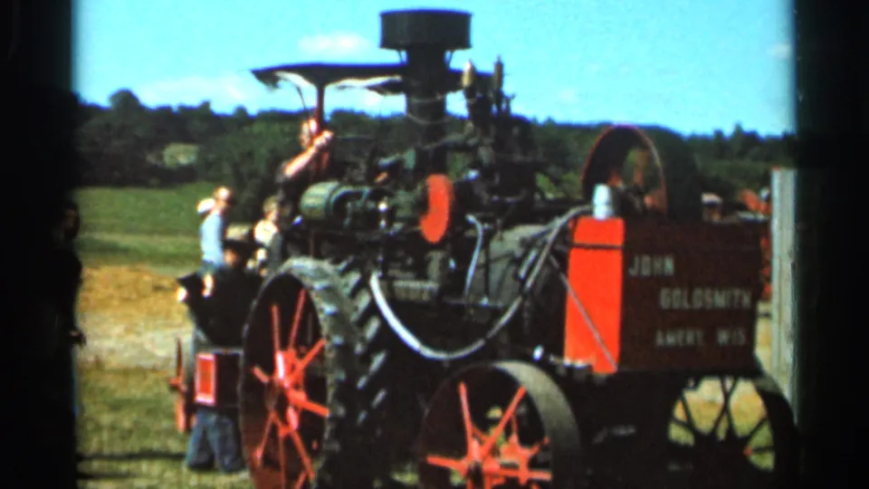 Red John Goldsmith steam tractor with large spoked wheels emits smoke as spectators watch in a Wauseon, Ohio field.