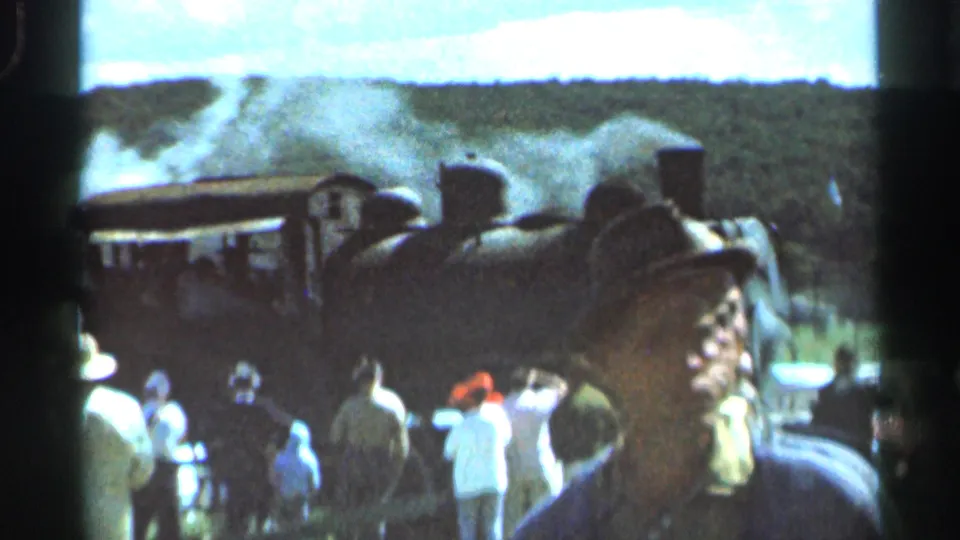 A man in a dark hat faces the camera while the Wauseon steam locomotive and gathered crowd remain visible in the background.