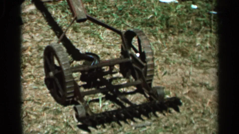 Lower-angle 8mm frame of the 1966 Wauseon, Ohio mower shot, emphasizing the paired wheels, cutting blades, and hand-pushed frame.