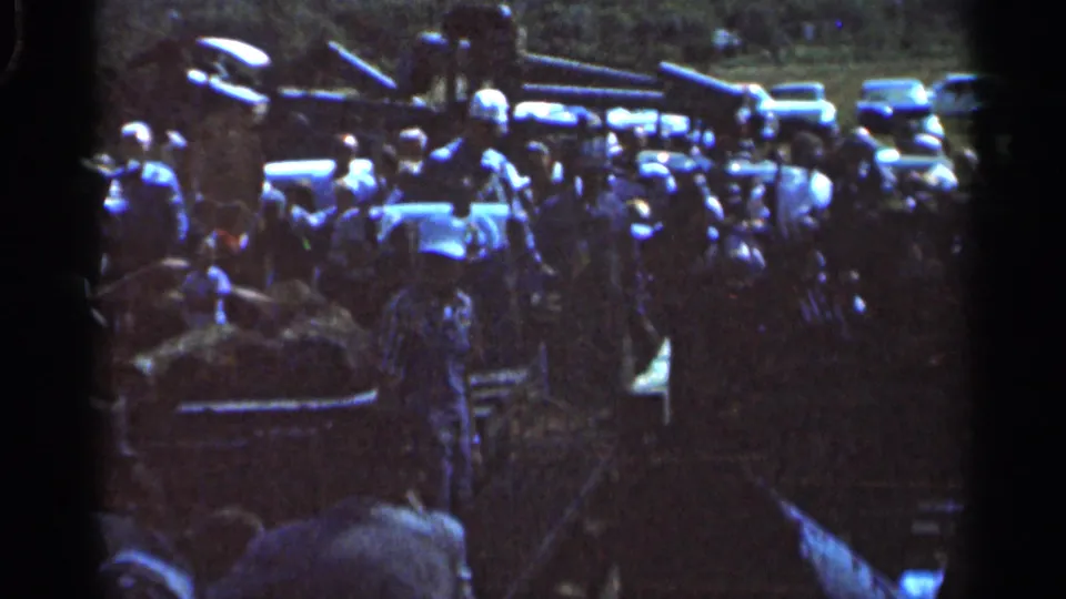 Adults in a Wauseon, Ohio field appear near a conveyor or lift structure, with parked vehicles and trees behind them.