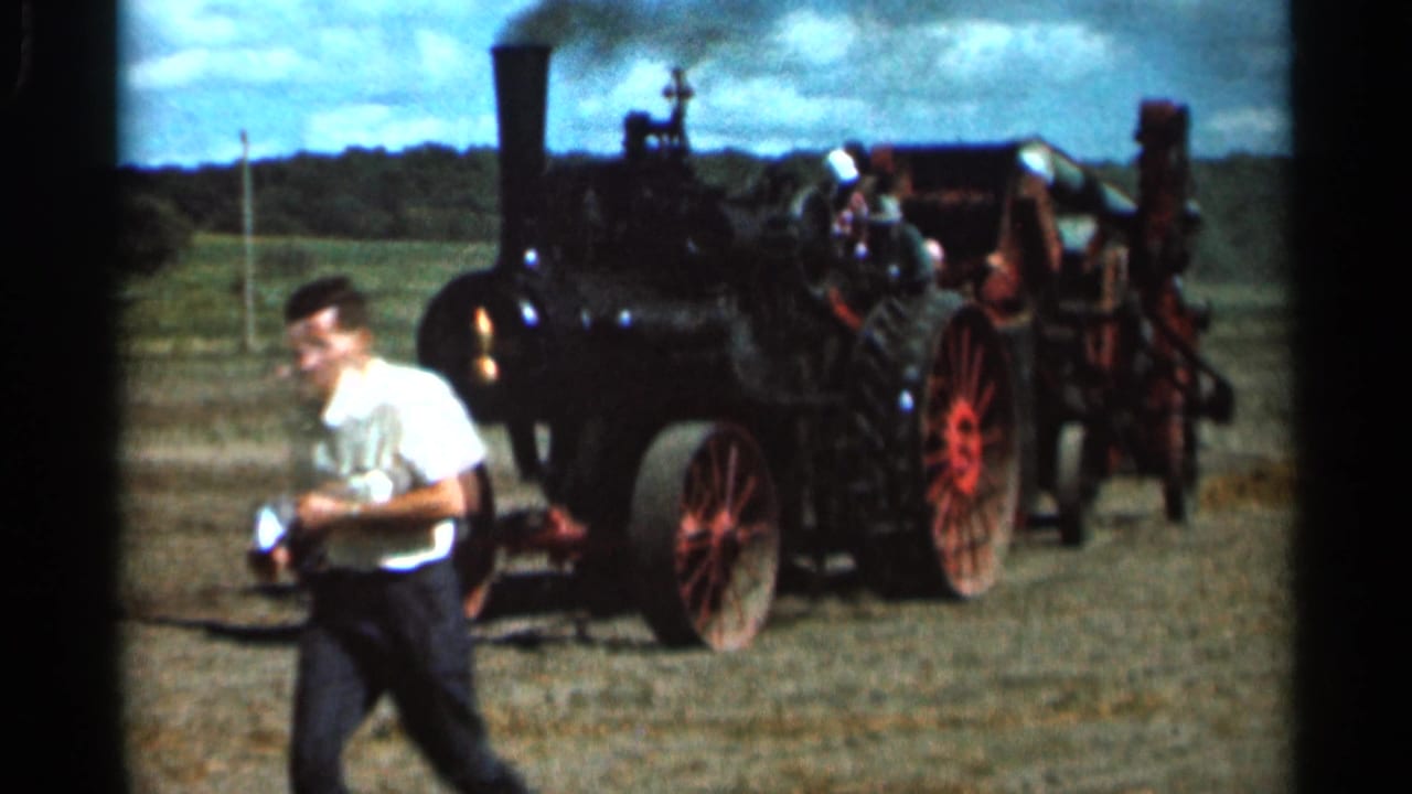 Young man walks past a smoking steam tractor in an open field.