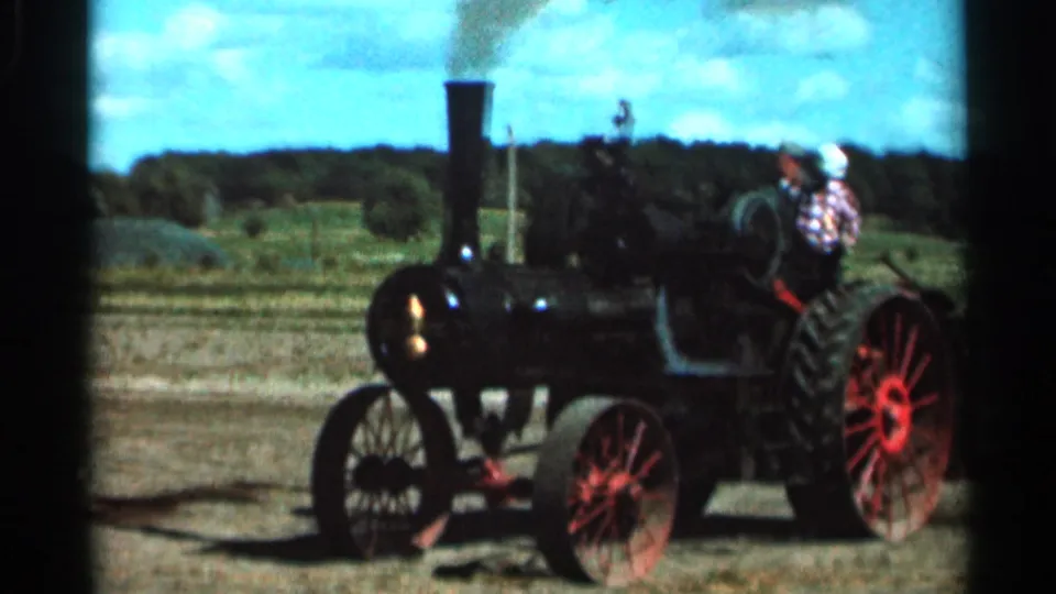 The 1966 Wauseon, Ohio clip shows a man at the controls of a black steam tractor with red wheels in an open rural field.