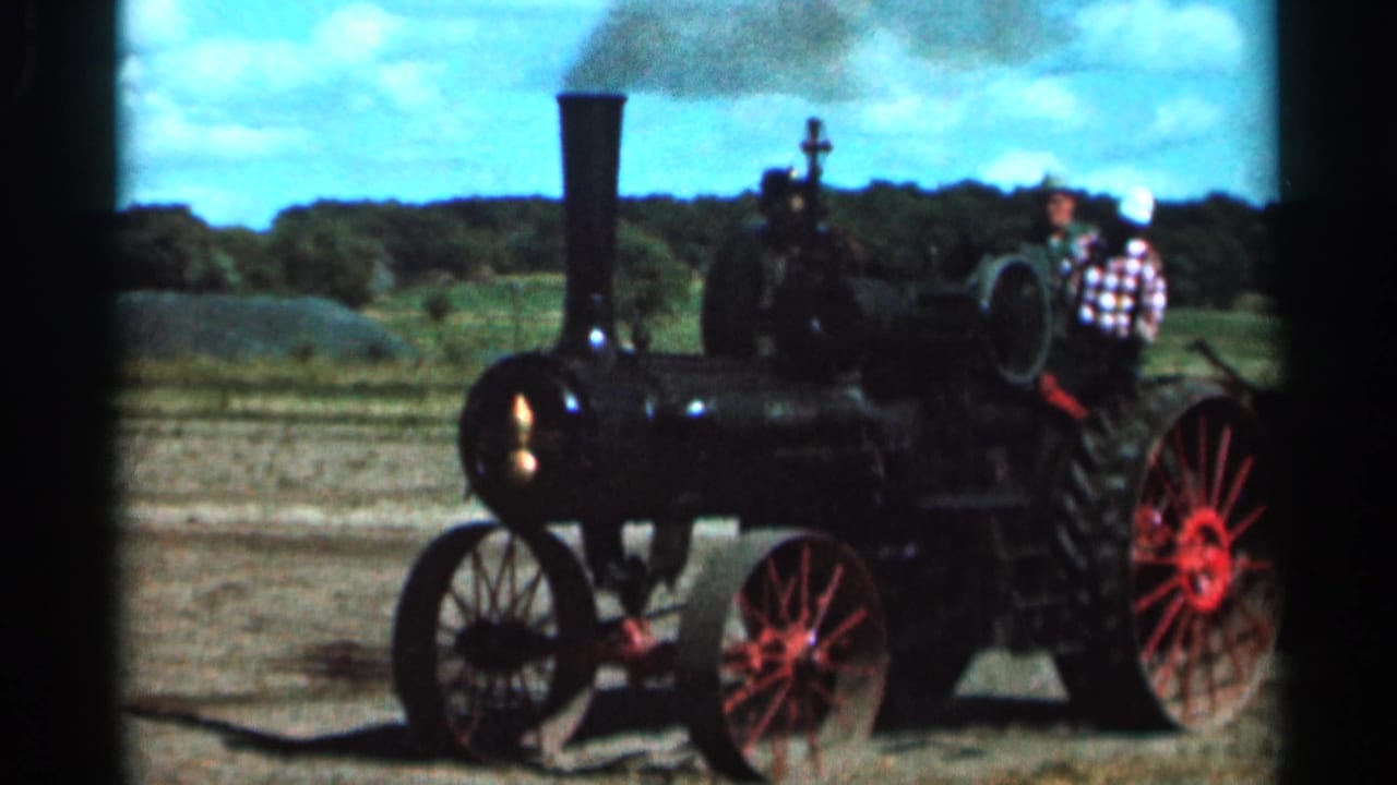 Steam tractor with red wheels in a field under a blue sky.