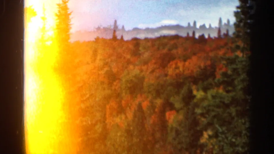 1966 8mm home-movie frame from Wauseon, Ohio showing fall-colored trees, evergreens, distant hills, and strong edge flare.