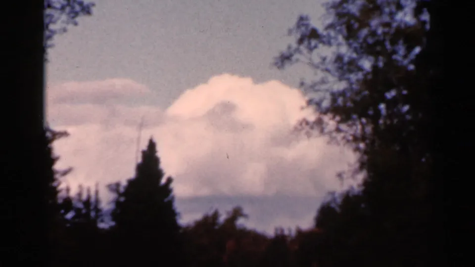 1966 Wauseon, Ohio 8mm frame with white clouds, distant hills, dark tree silhouettes, and autumn-colored trees below.