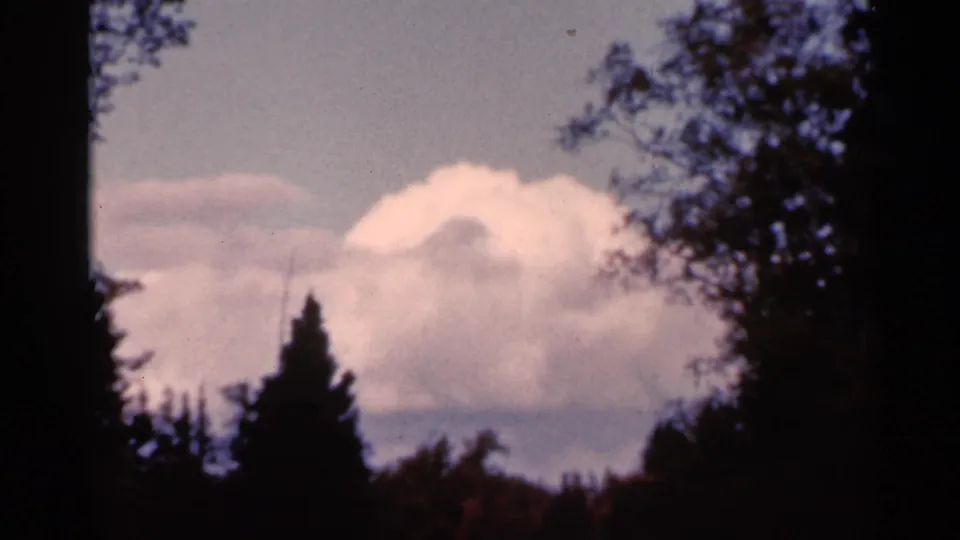 1966 Wauseon, Ohio 8mm frame showing a soft cloud formation framed by dark foreground trees.
