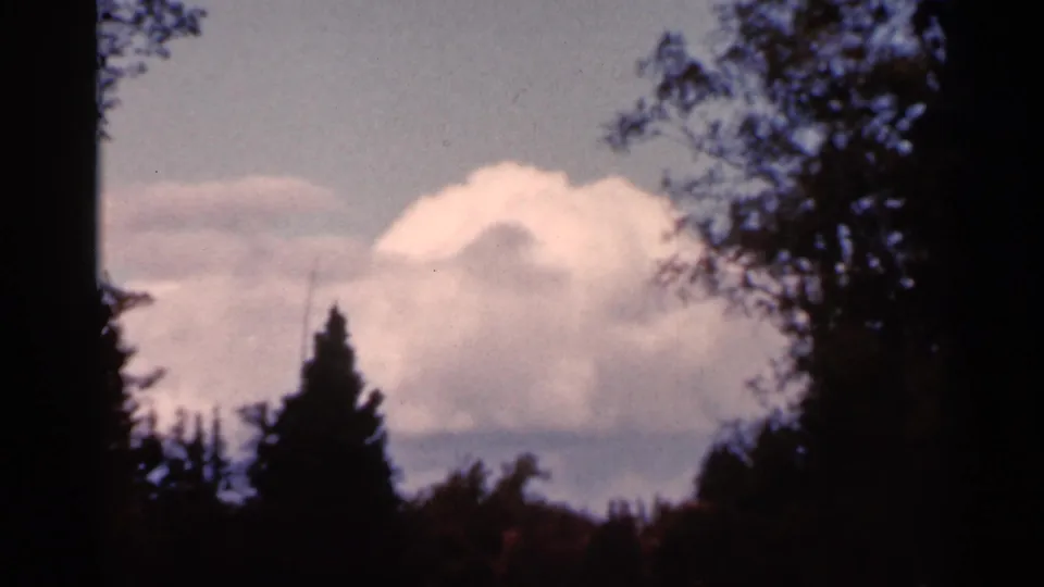 A soft 8mm view of clouds and sky framed by shadowed trees, identified by metadata as Wauseon, Ohio in 1966.